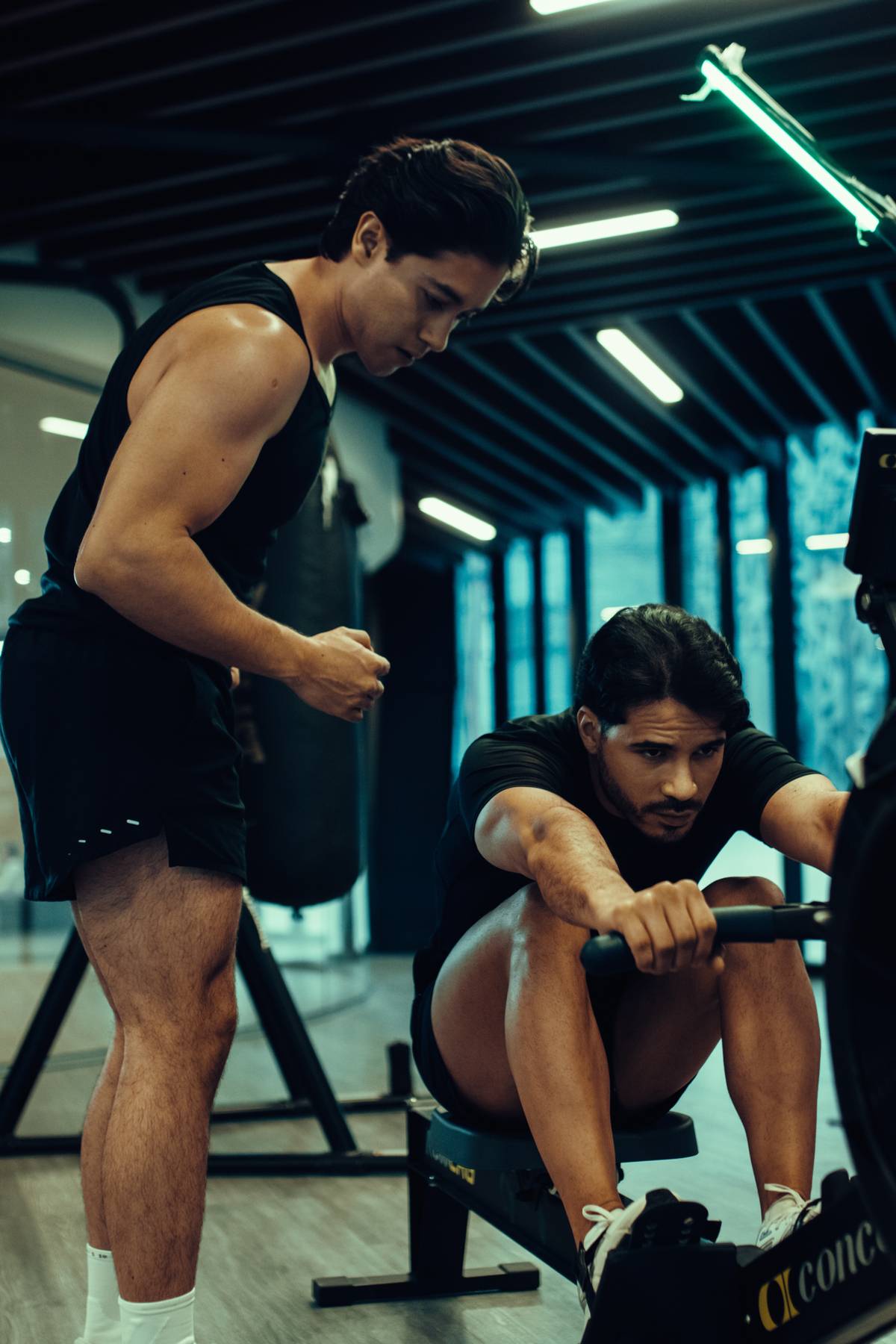 Coach asistiendo a un alumno en el remo durante una sesión de entrenamiento híbrido